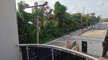A balcony with a metal railing overlooking a street with buildings and greenery.