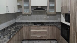 Eine Küche mit Marmorarbeitsplatten, Holzschränken, einem eingebauten Backofen und einer Dunstabzugshaube.