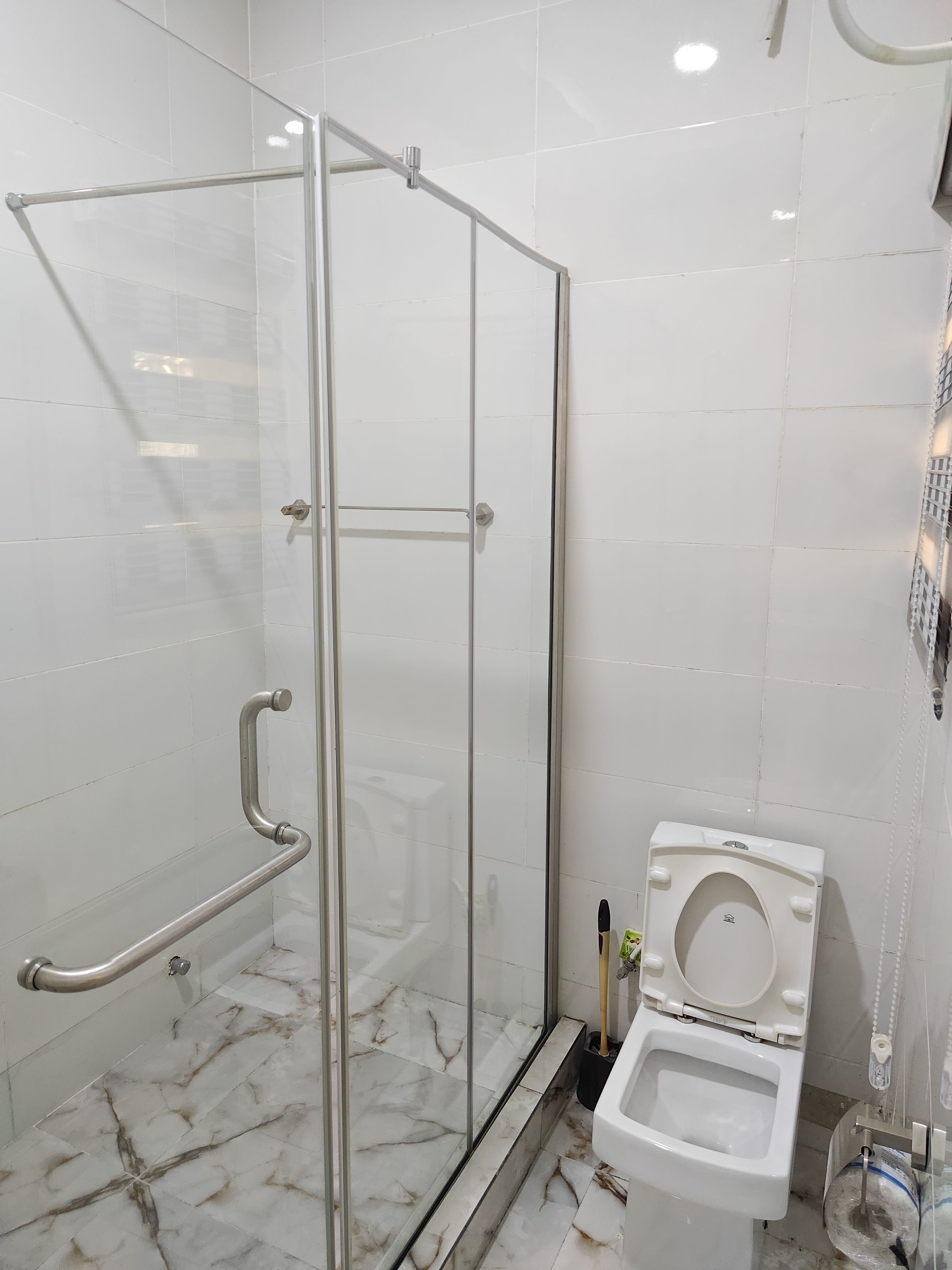 Un baño con ducha envuelta en vidrio, inodoro blanco y suelo de mármol.