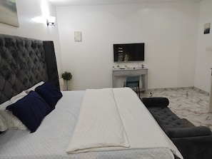 A bedroom with a bed, a desk, a chair, and a television.