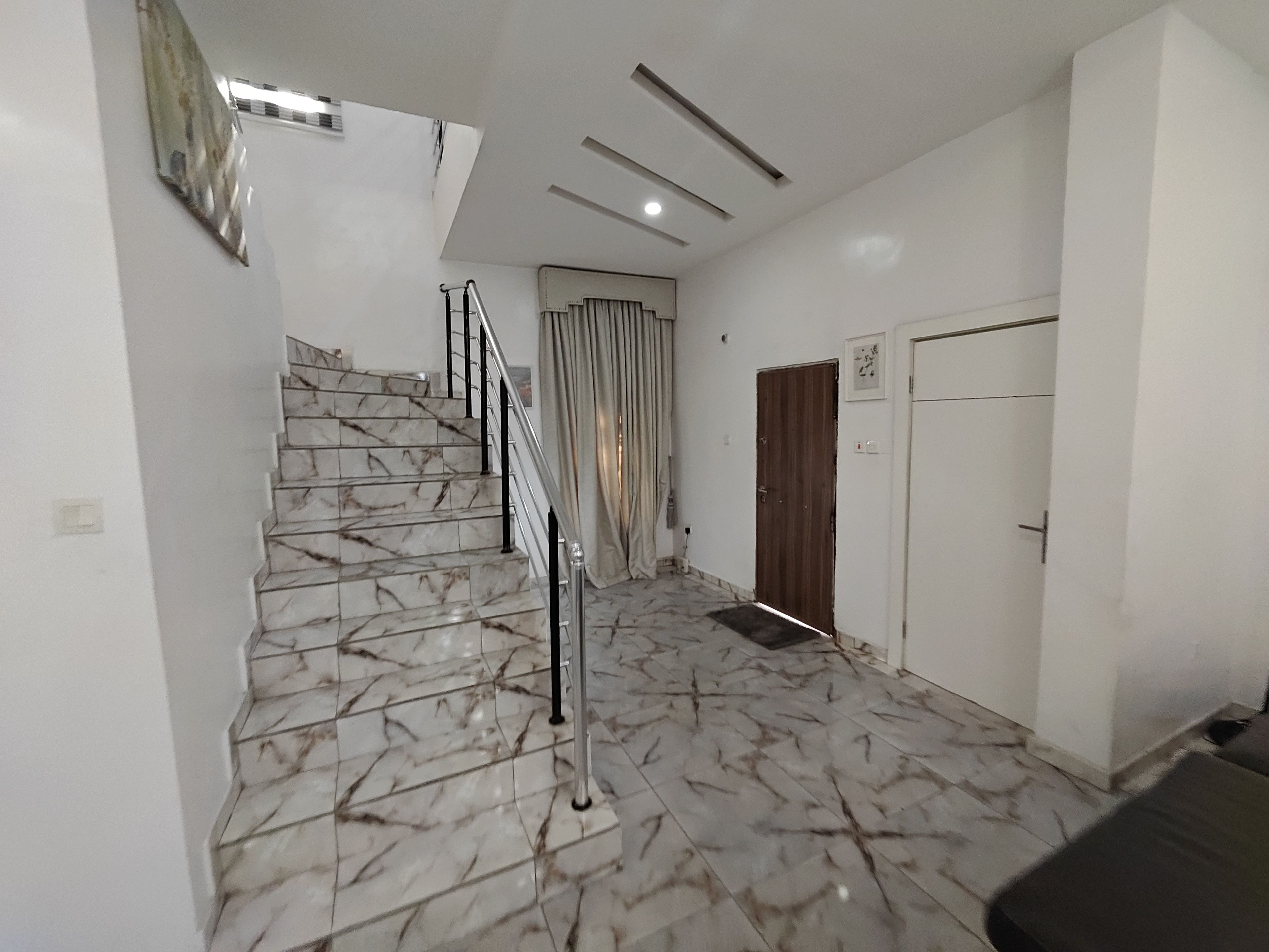 A staircase with marble steps and a metal railing, leading to a room with a door and a light switch on the wall.