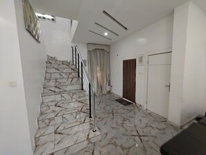 A staircase with marble steps and a metal railing, leading to a room with a door and a light switch on the wall.