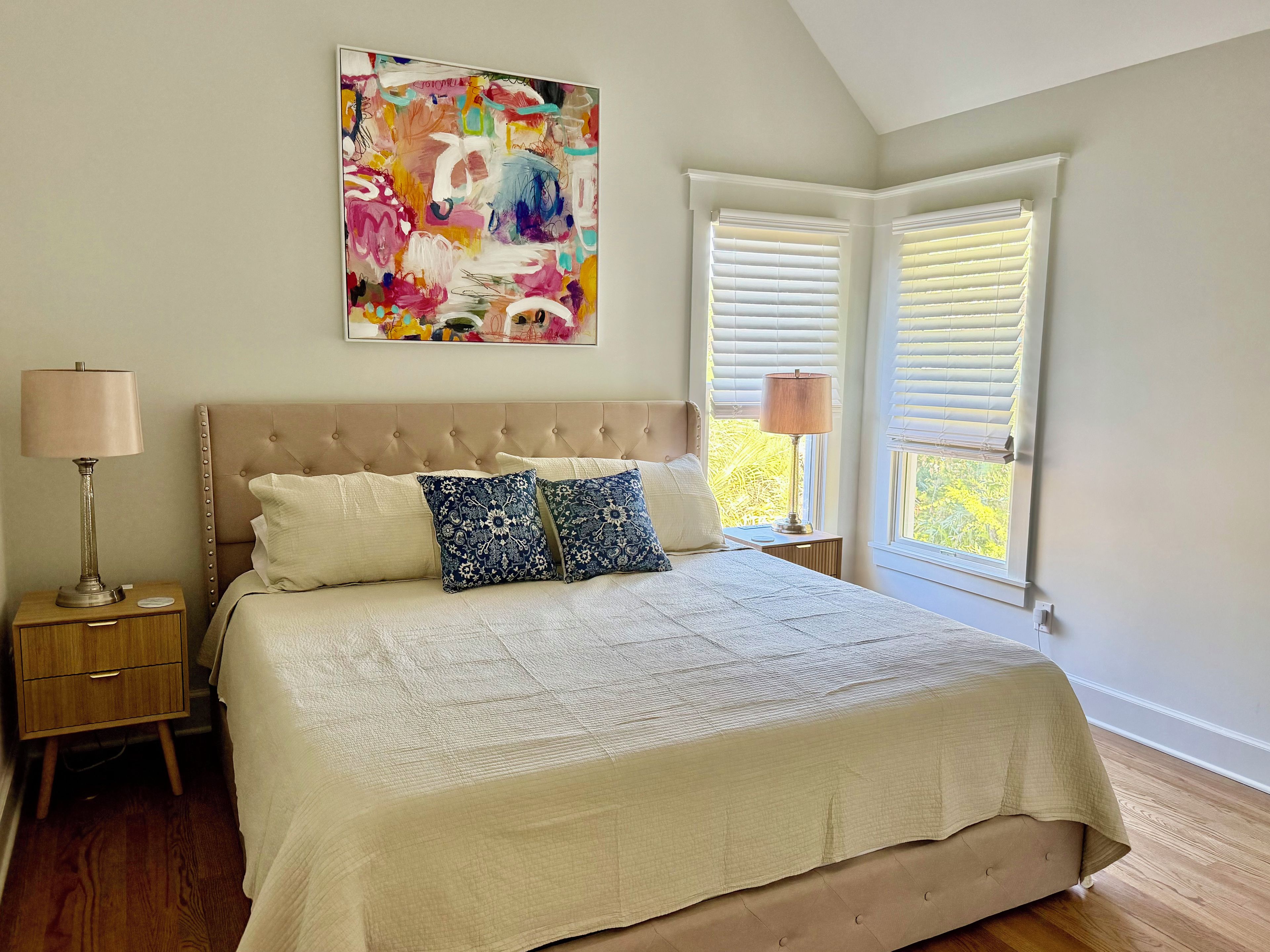 Un dormitorio con una cama grande, dos lámparas de noche, una mesita de noche y un cuadro abstracto colorido en la pared.