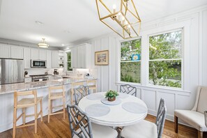 Une cuisine moderne avec des meubles blancs, un îlot central et un coin repas comprenant une table ronde et des chaises.