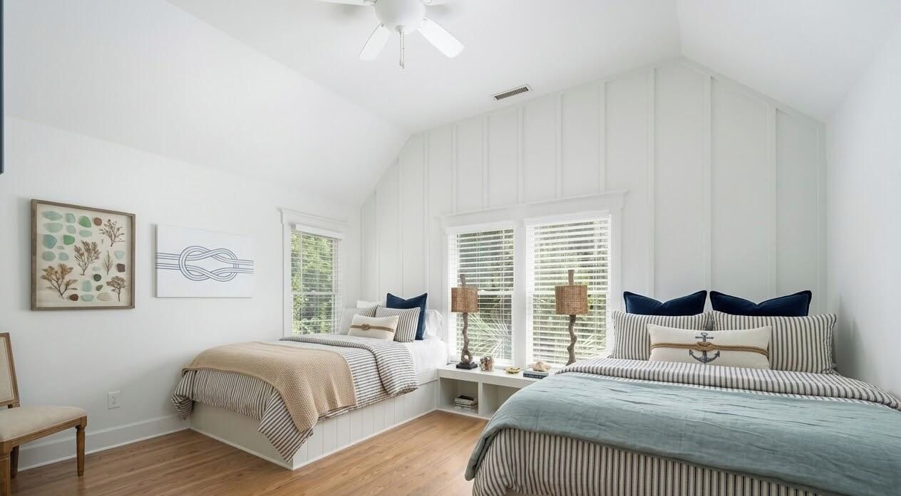 A bedroom with two beds, a ceiling fan, and a window with blinds.