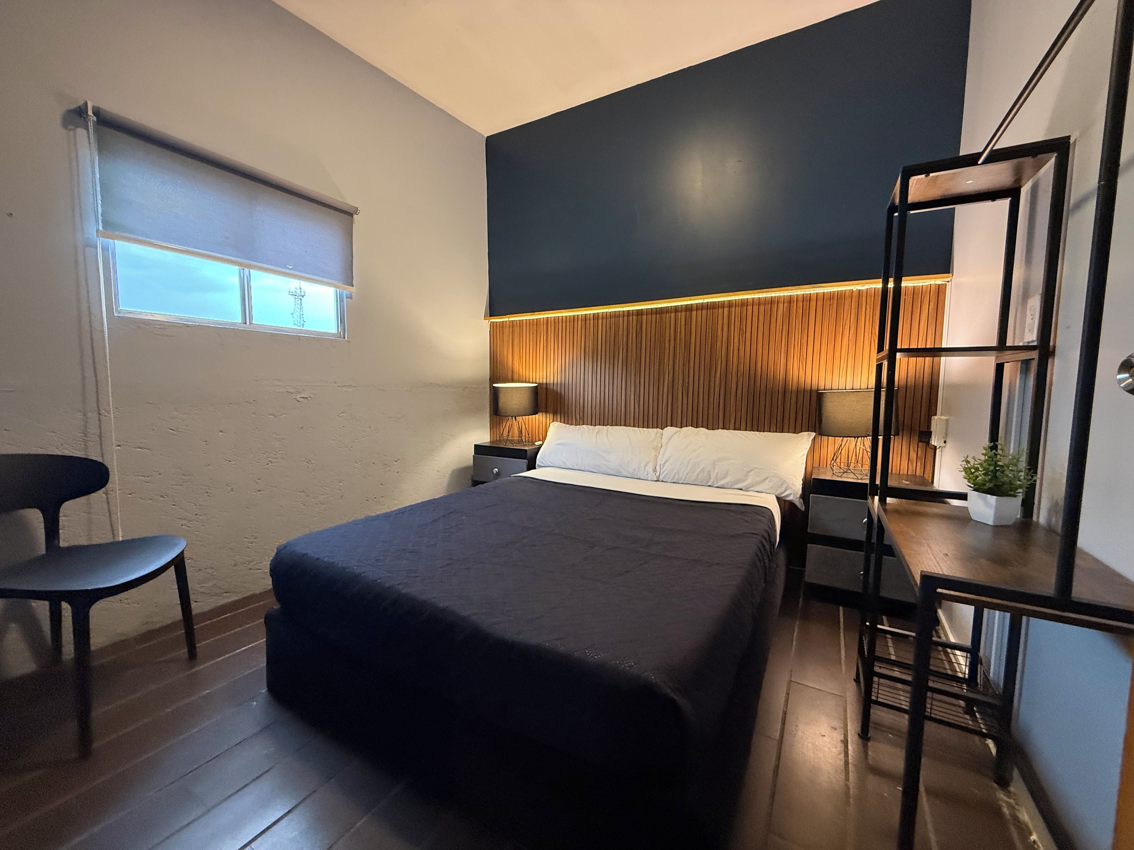 A modern bedroom with a bed, bedside tables, a chair, a window, and a plant.