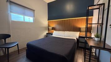 A modern bedroom with a bed, bedside tables, a chair, a window, and a plant.