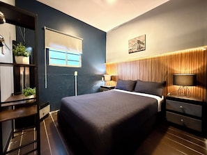Quarto moderno com uma cama grande, mesas de cabeceira, janela com persianas, prateleira fixada na parede com plantas e um quadro emoldurado.