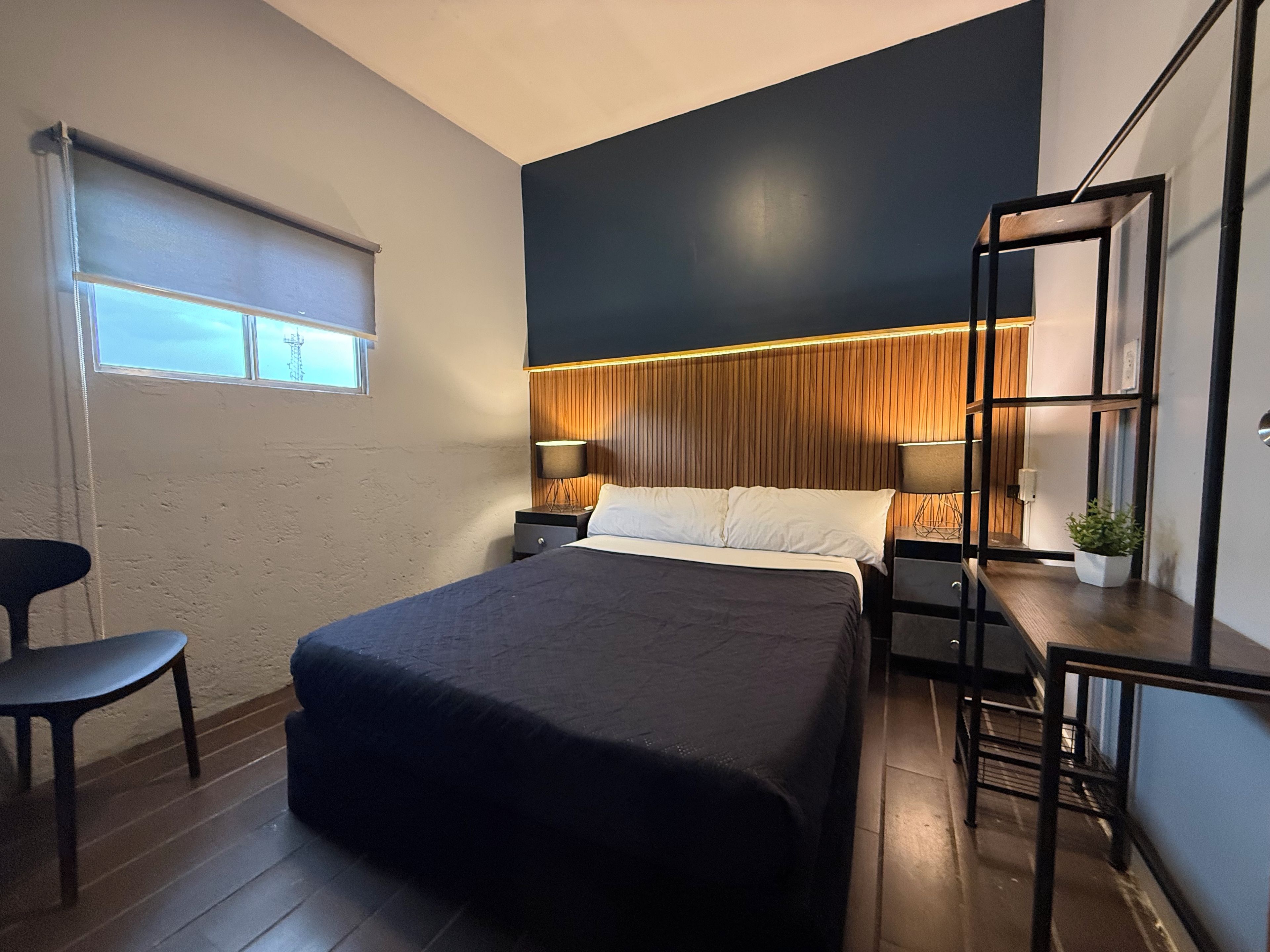 Een moderne hotelkamer met een bed, nachtkastjes, een stoel, een raam met zonwering en een houten accentmuur.