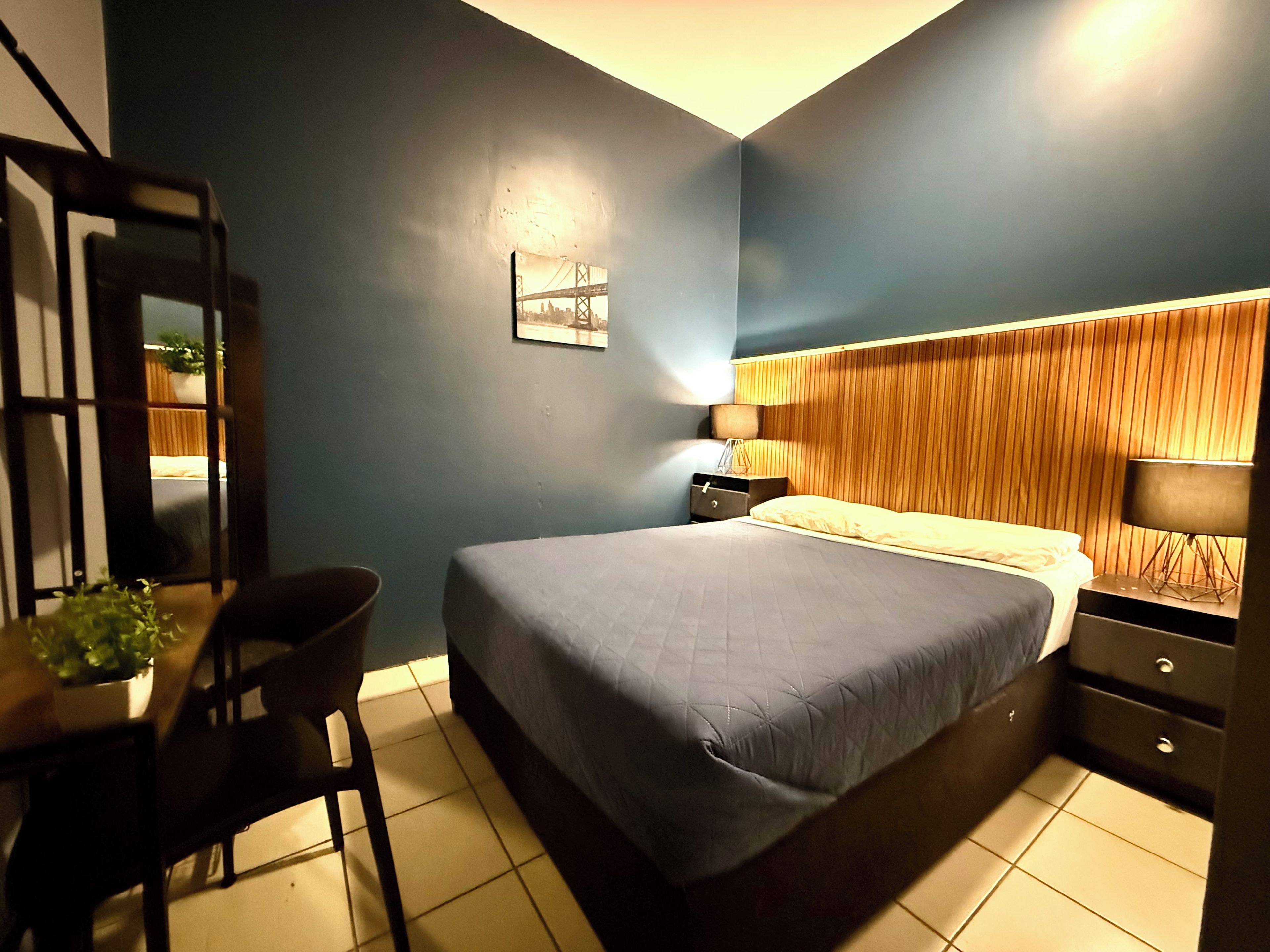 A hotel room with a bed, bedside table, lamp, and a wall-mounted picture.