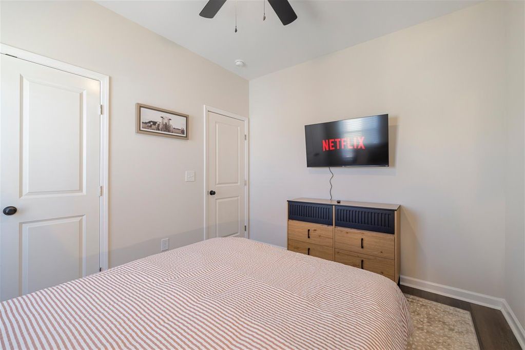 A bedroom with a bed, a TV mounted on the wall, a dresser, and a door.