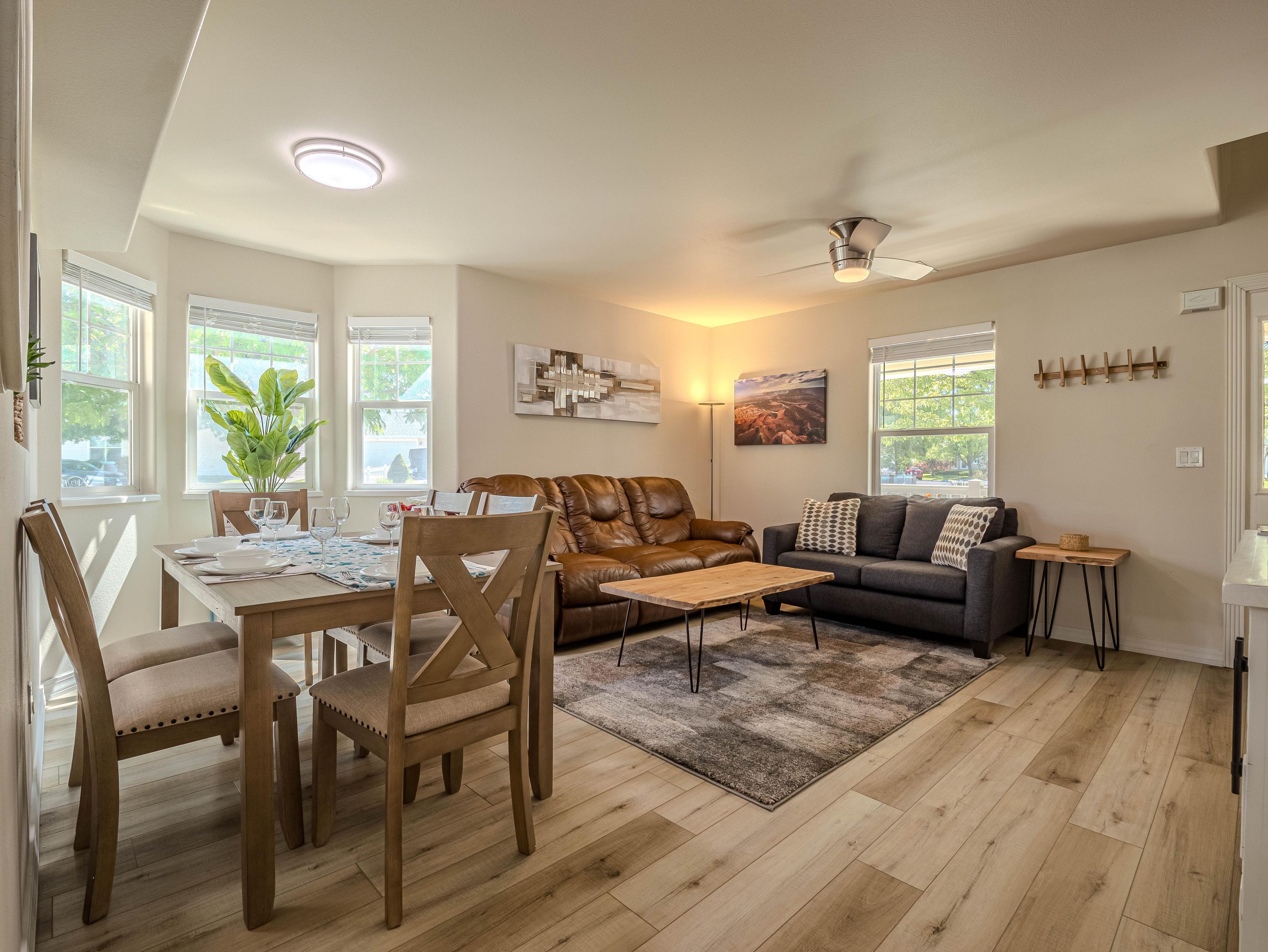 A living room with a dining area, a ceiling fan, and a large window with blinds.