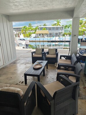 A covered outdoor seating area with wicker furniture and a view of a pool and buildings in the background. - Coastal 1 Bedroom Unit with 40 foot boat slip (Tavernier)