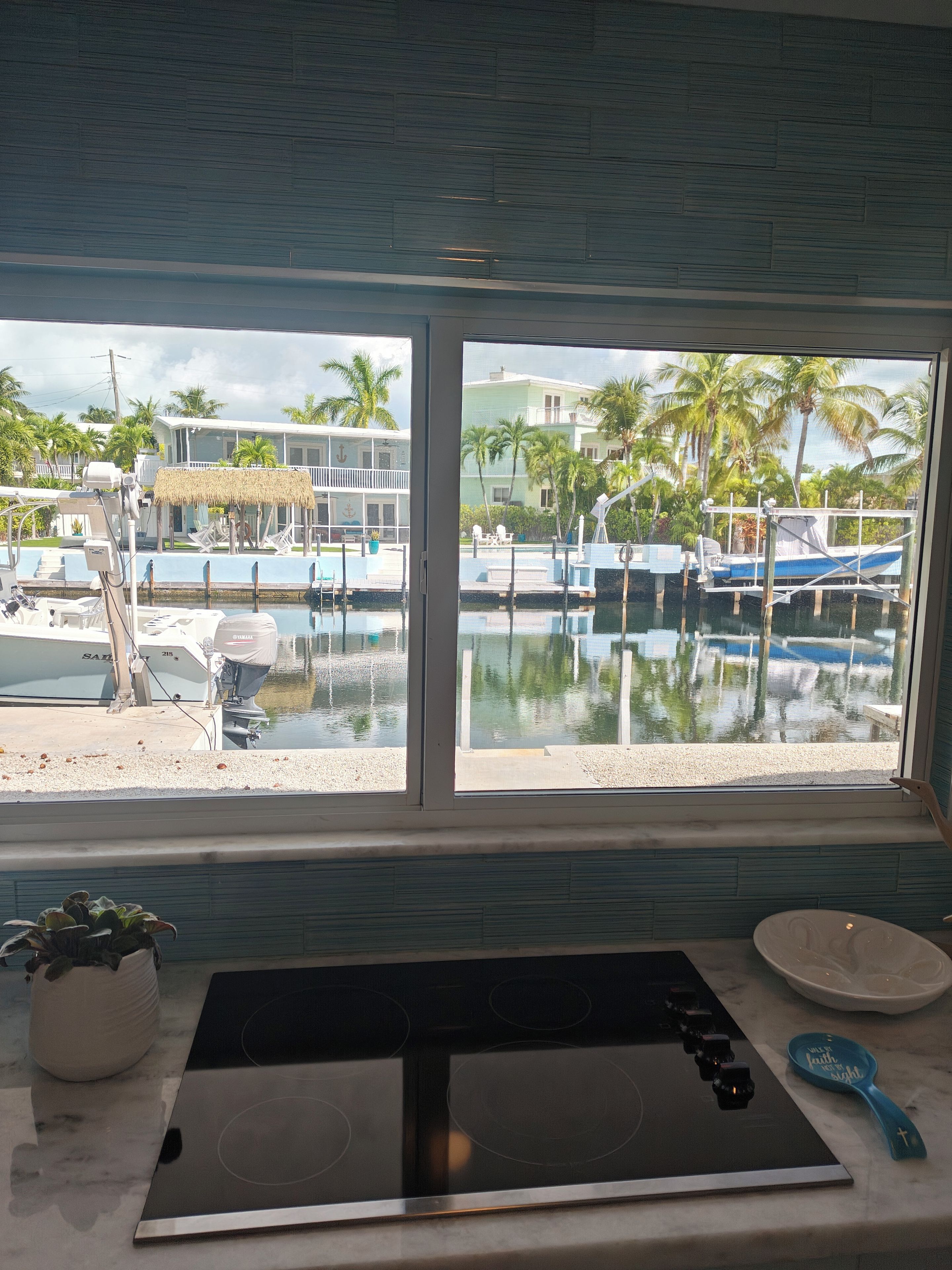 A kitchen with a large window overlooking a marina with boats and palm trees.