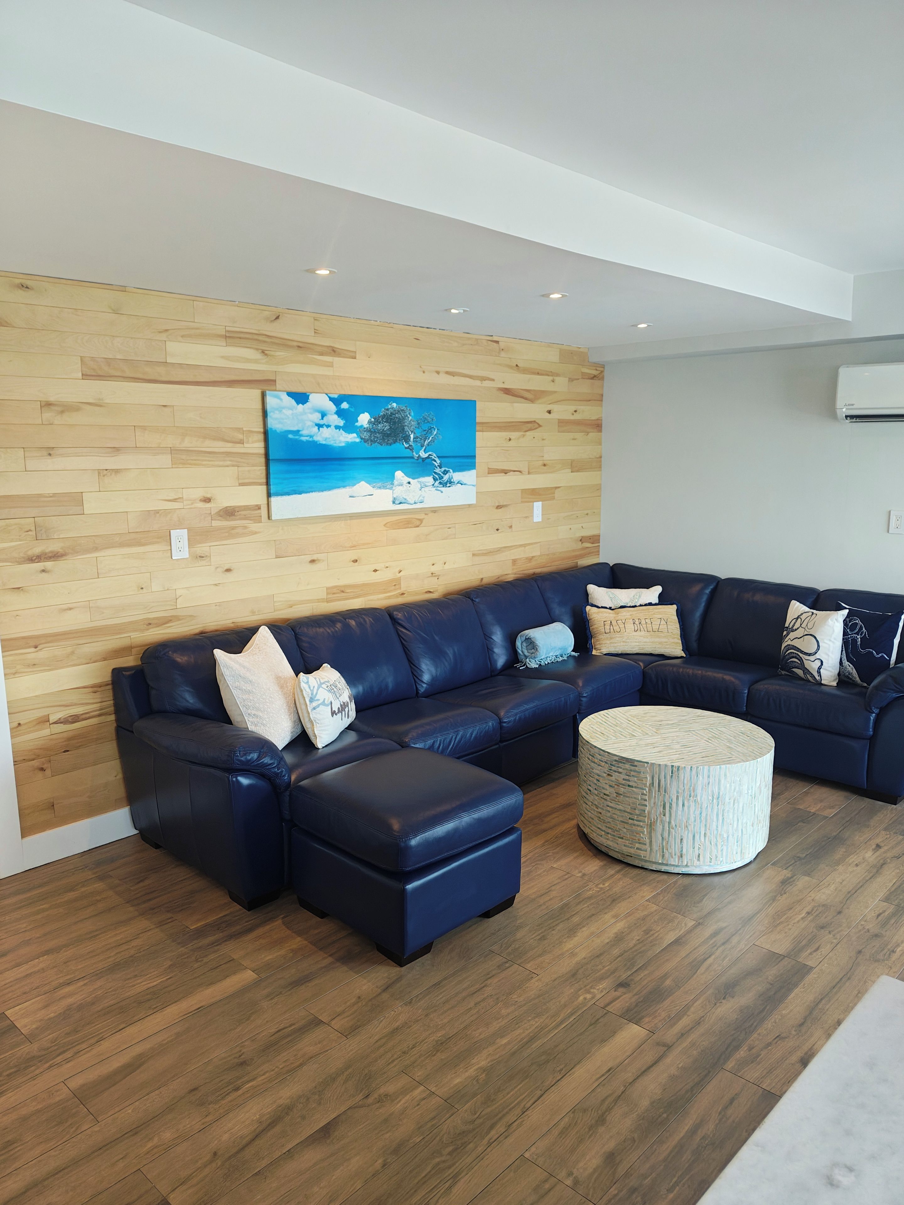 Uma sala de estar moderna com um sofá seccional, uma mesa de centro redonda e uma parede de madeira com uma pintura.