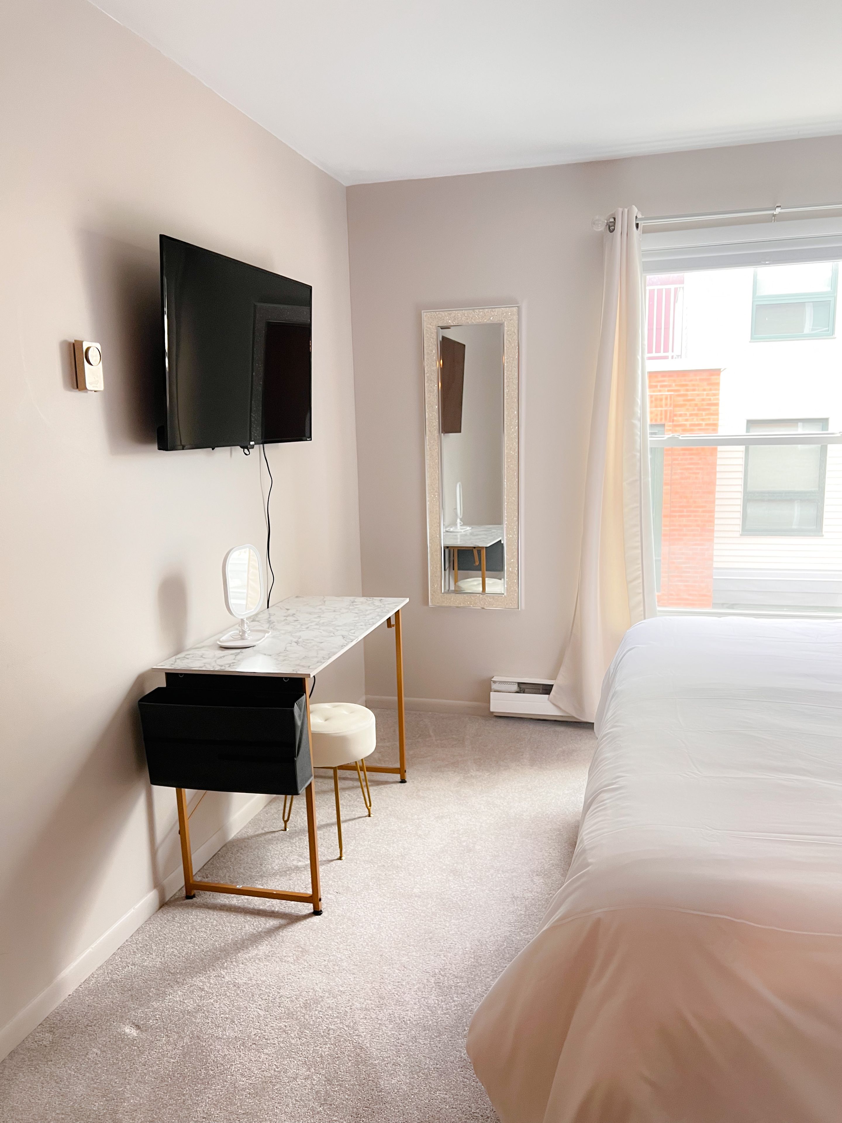 Une chambre d’hôtel comprenant un lit, un bureau avec un miroir, un téléviseur fixé au mur et une fenêtre avec des rideaux.