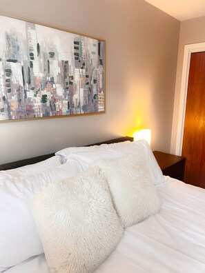 Une chambre d’hôtel avec un lit, des oreillers blancs, un tableau au mur et une table de chevet avec une lampe.