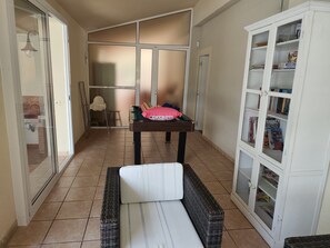 A room with a bed, a small table with a pink pillow, a wicker chair, a cabinet with books, and a sliding glass door leading to a bathroom. - Beautiful villa with a garden and pool near the beach (CT)