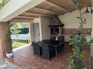 Eine Terrasse im Freien mit Terrakottafliesen, einem Tisch mit Glasplatte und schwarzen Korbstühlen.