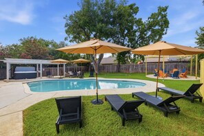 A backyard with a swimming pool, lounge chairs, and umbrellas. - Resort Getaway: Pool, Hot Tub & Putting Green (San Antonio)