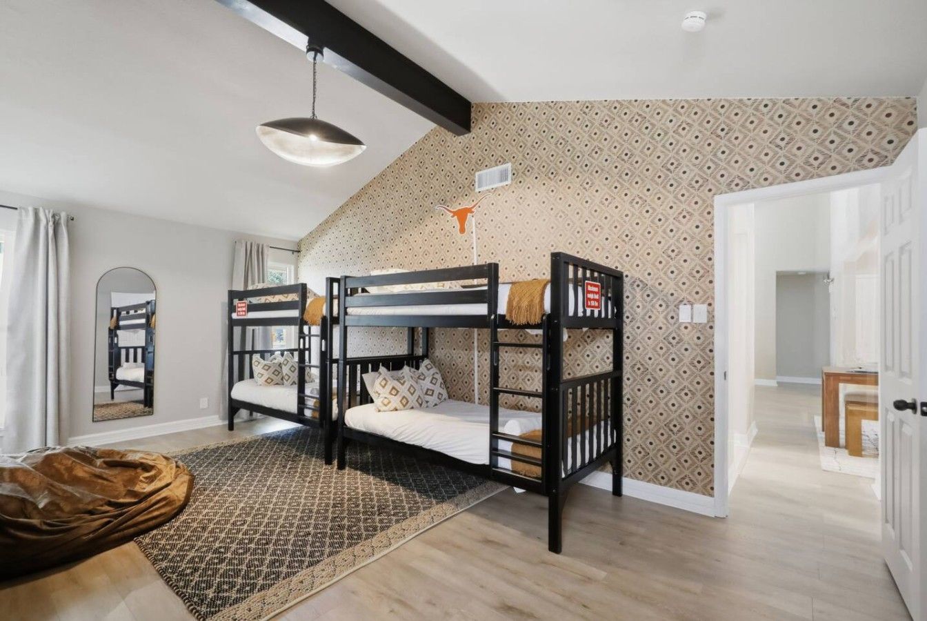 A room with bunk beds, a patterned wall, a hanging light fixture, and a rug.