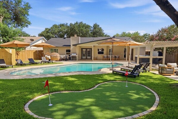 A backyard with a swimming pool, lounge chairs, and a covered patio area. - Resort Getaway: Pool, Hot Tub & Putting Green (San Antonio)