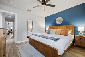 A bedroom with a wooden bed, a ceiling fan, a nightstand with a lamp, a mirror on the wall, and a hallway leading to another room. - Resort Getaway: Pool, Hot Tub & Putting Green (San Antonio)