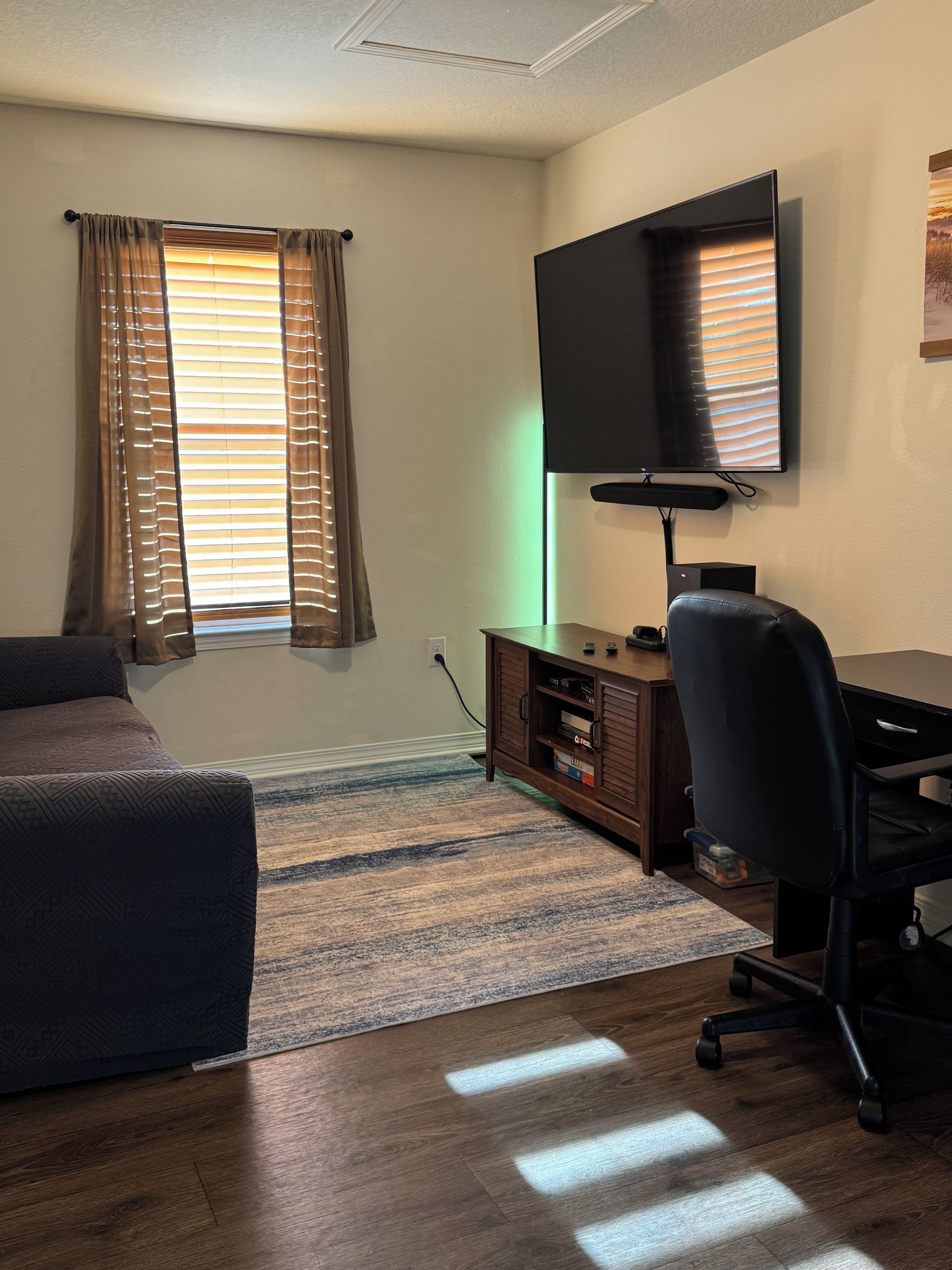 A room with a bed, a desk with a chair, a television, and a window with curtains.
