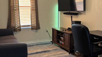 A room with a bed, a desk with a chair, a television, and a window with curtains.