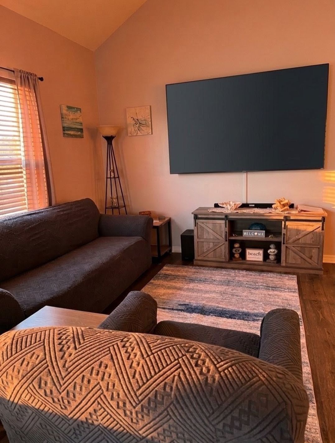 Un salon comprenant un canapé, un pouf et un téléviseur à écran plat fixé au mur.