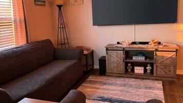 Un salon comprenant un canapé, un pouf et un téléviseur à écran plat fixé au mur.
