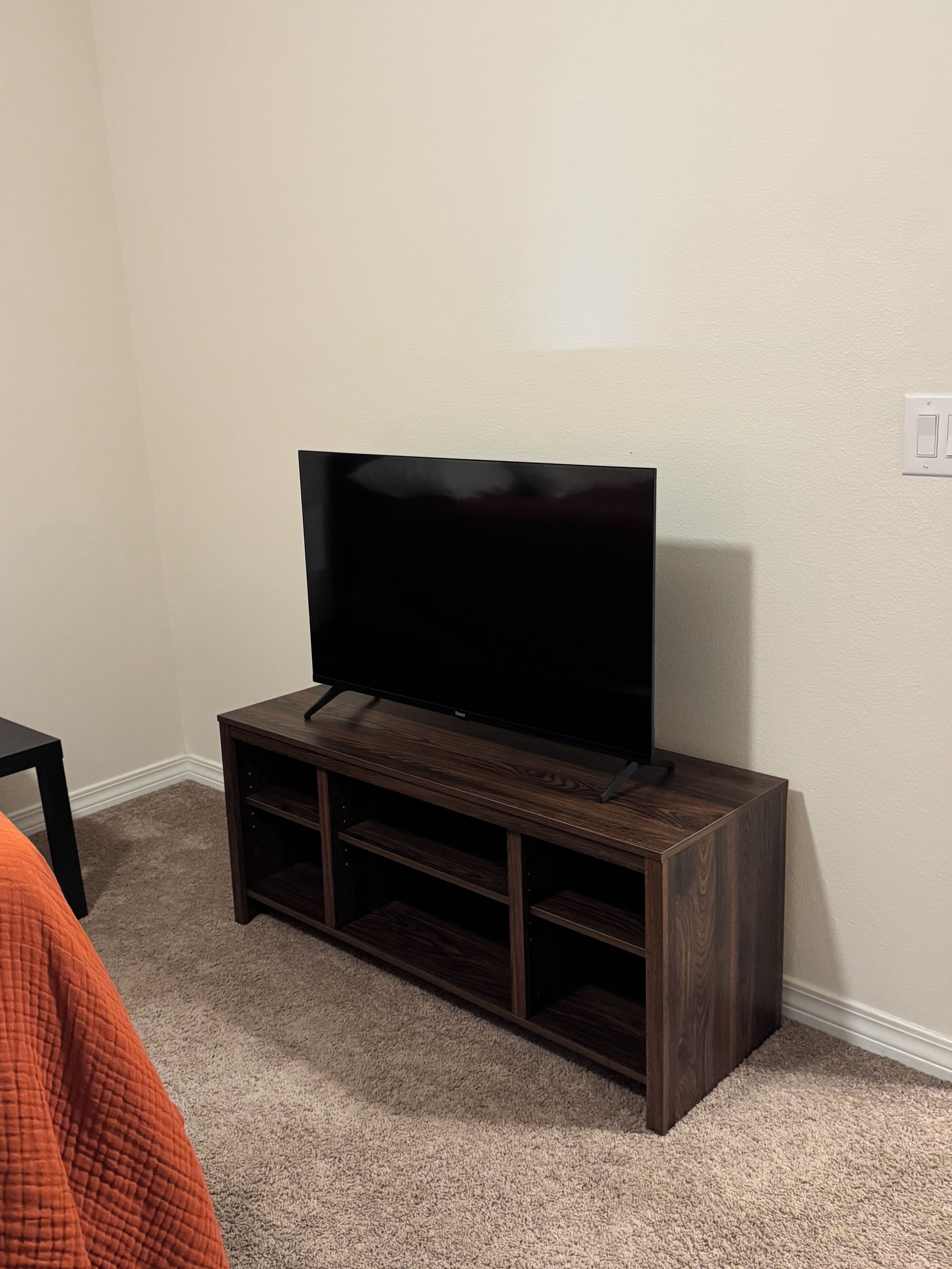 A television on a wooden stand in a room with carpeted flooring and a plain wall.