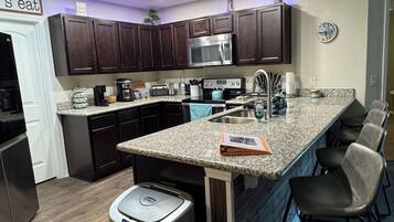 A modern kitchen with dark wood cabinets, stainless steel appliances, a granite countertop, and a trash can.