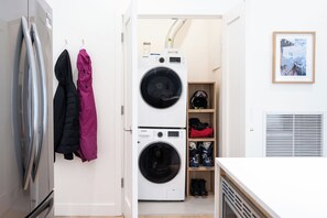 A laundry room with a front-loading washer and dryer, a coat rack with jackets, and a framed picture on the wall. - The Chando (Revelstoke)