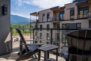 A balcony with a view of mountains, a glass railing, and outdoor furniture. - The Chando (Revelstoke)