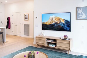 A modern living room with a flat-screen TV, a wooden cabinet with books, and a vase with flowers on a wooden table. - The Chando (Revelstoke)