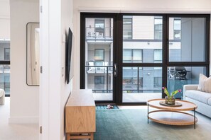 A modern living room with a large sliding glass door leading to an outdoor balcony, a wooden side table, a round wooden coffee table with a vase of flowers, and a white sofa. - The Chando (Revelstoke)