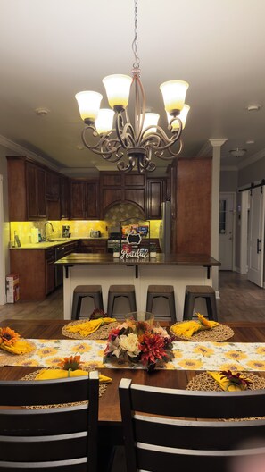 A modern kitchen with a central island, wooden cabinets, and a chandelier.