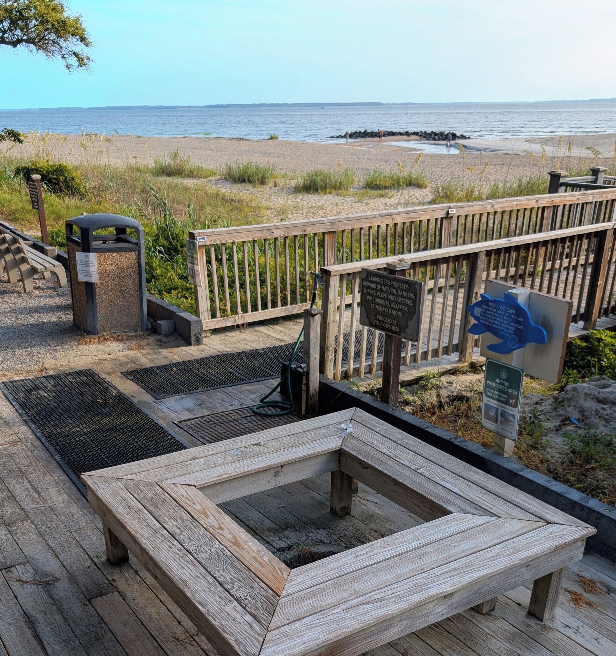 A wooden deck with a bench, a trash can, and a sign warning of natural dangers.
