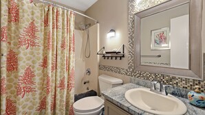 A bathroom with a shower curtain, toilet, sink, and a mirror with a decorative tile backsplash. - Steps to beach & pools  Cozy 2-bedroom 2 bath condo in Hilton Head Island (Hilton Head Island)