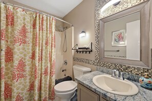 Et badeværelse med bruseforhæng, toilet, vask og et spejl med dekorative fliser bag sig.