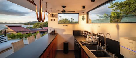A modern kitchen with a large window, a ceiling fan, and a view of the sea.