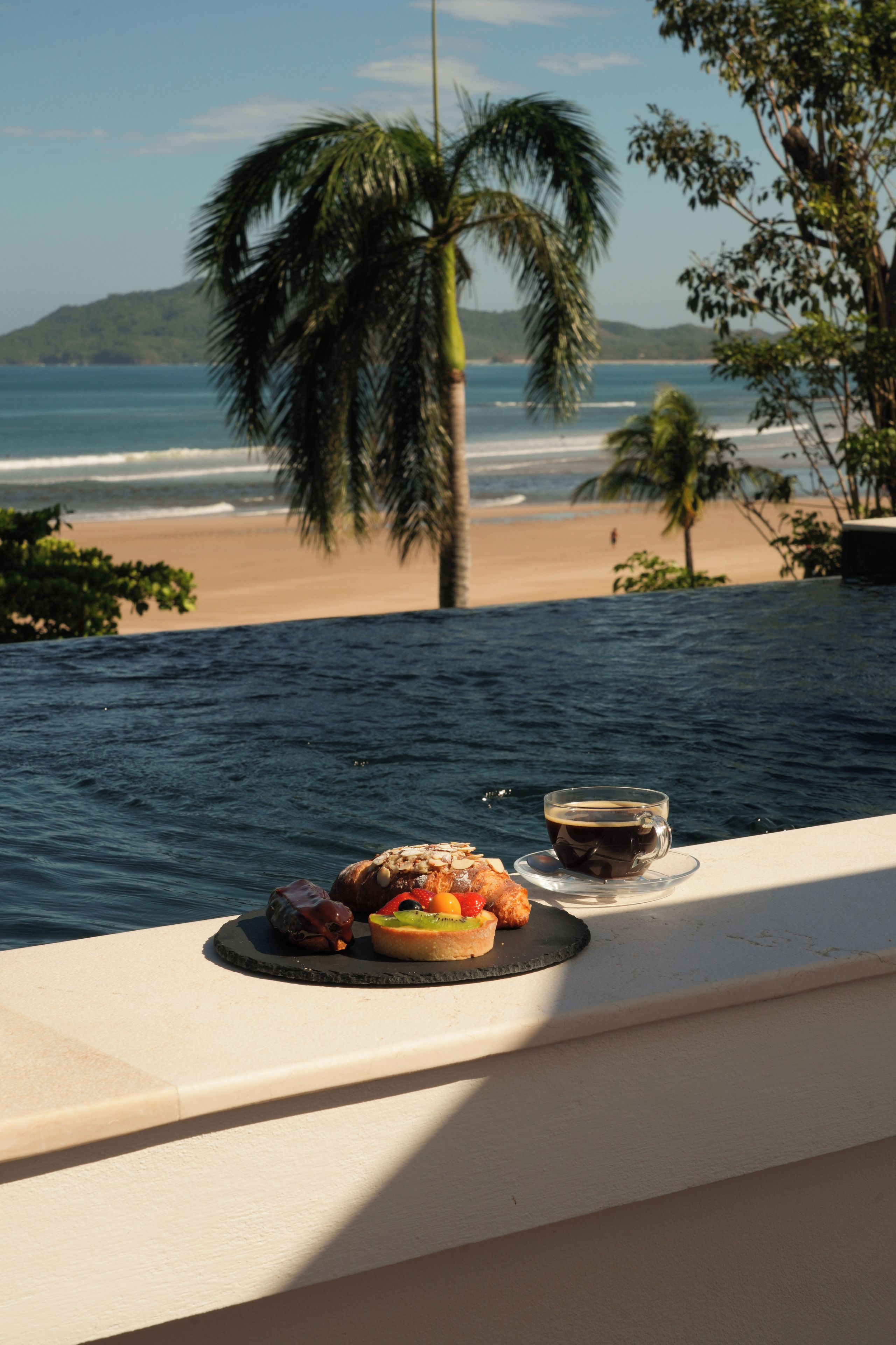 Una mesa de comedor con un plato de comida y una taza de café, con vistas a una playa y al océano.
