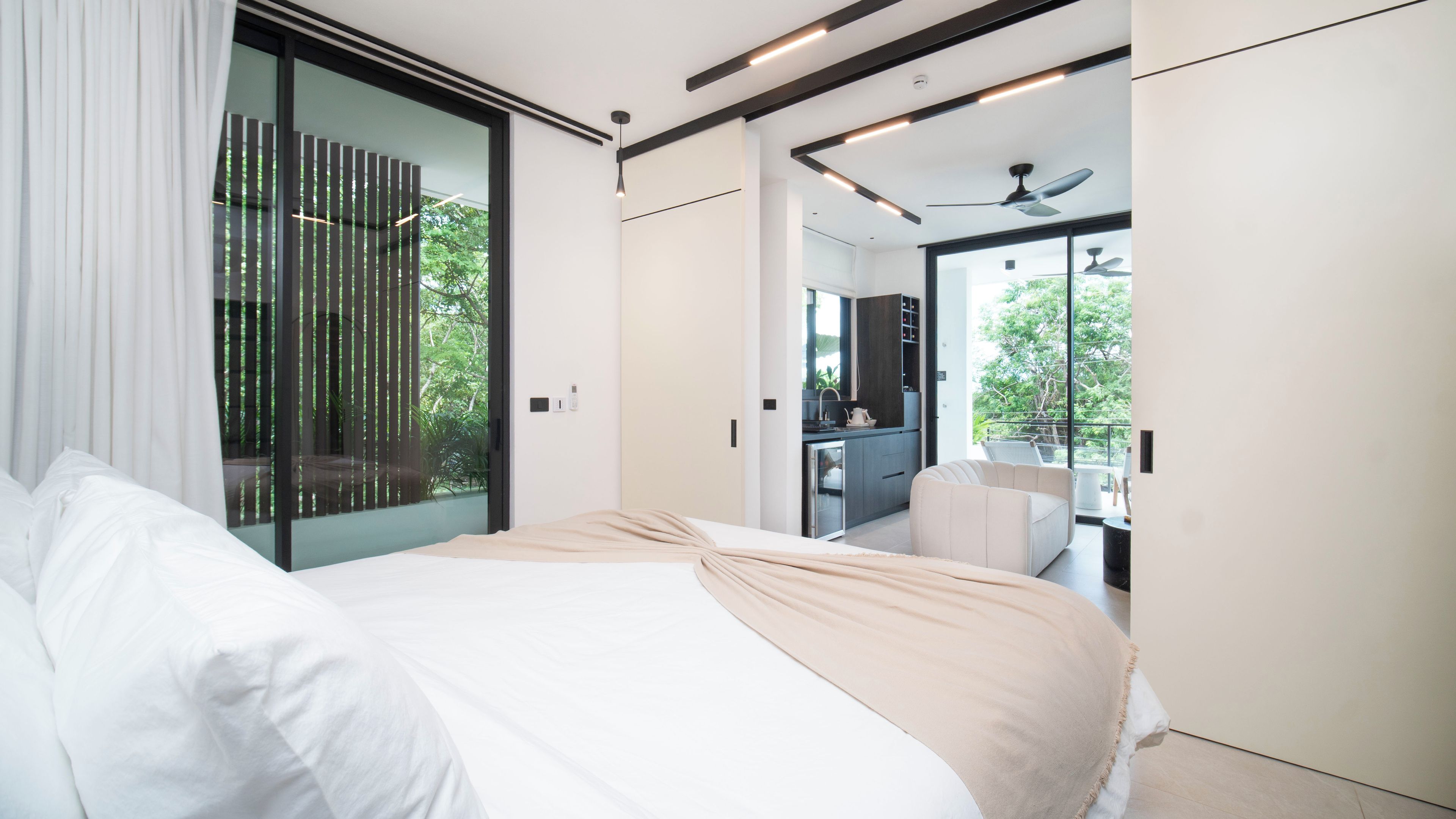 Un dormitorio moderno con una cama grande, un ventanal corredero que da a un balcón y vistas de una zona de cocina.