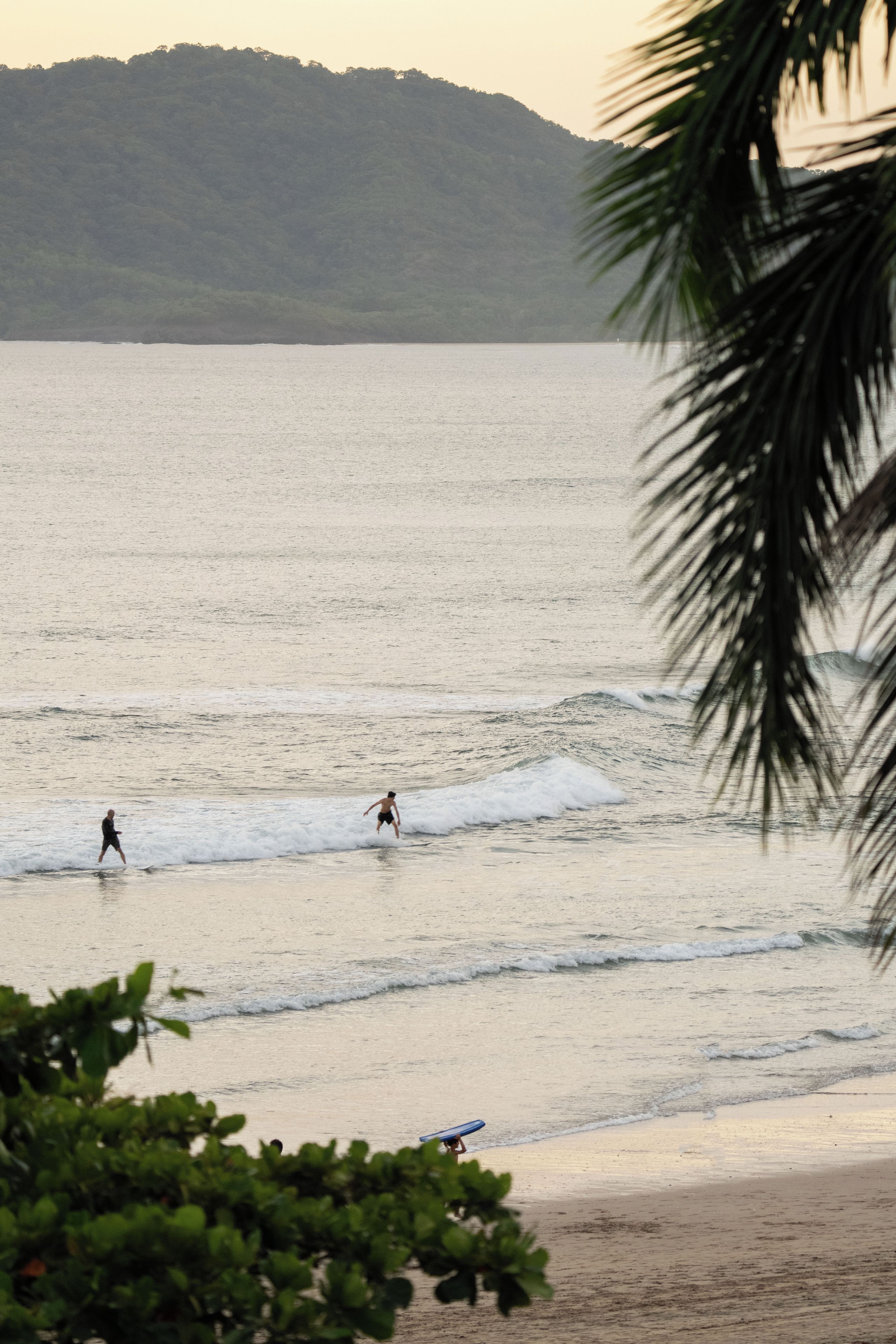 Una playa con olas, una persona caminando y una tabla de surf sobre la arena.