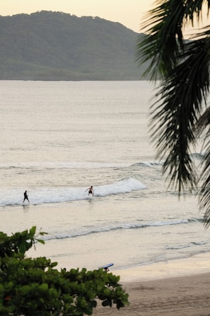 A beach with waves, a person walking, and a surfboard on the sand.