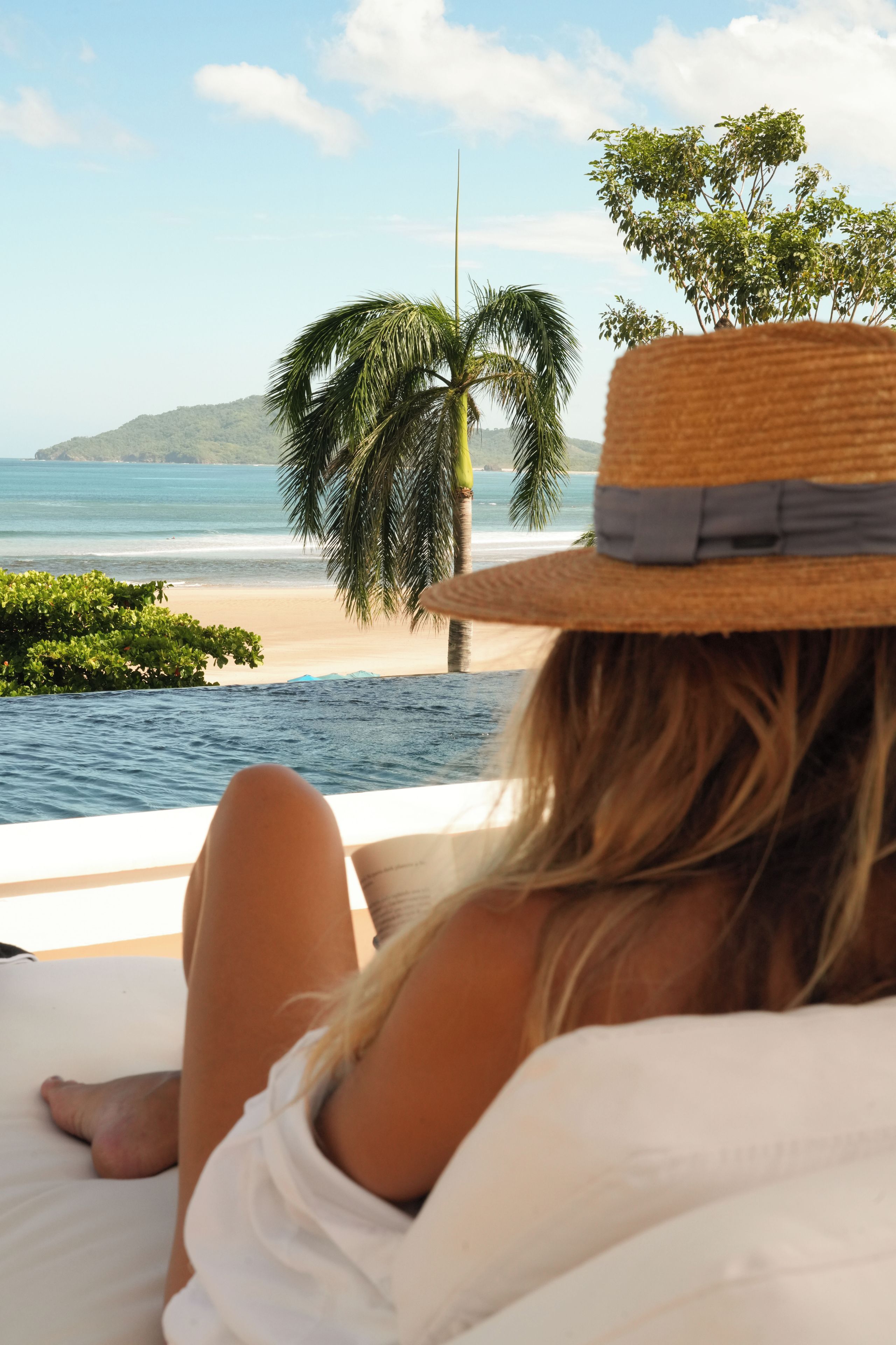 Una persona recostada en una cama con vistas a la playa y al océano.