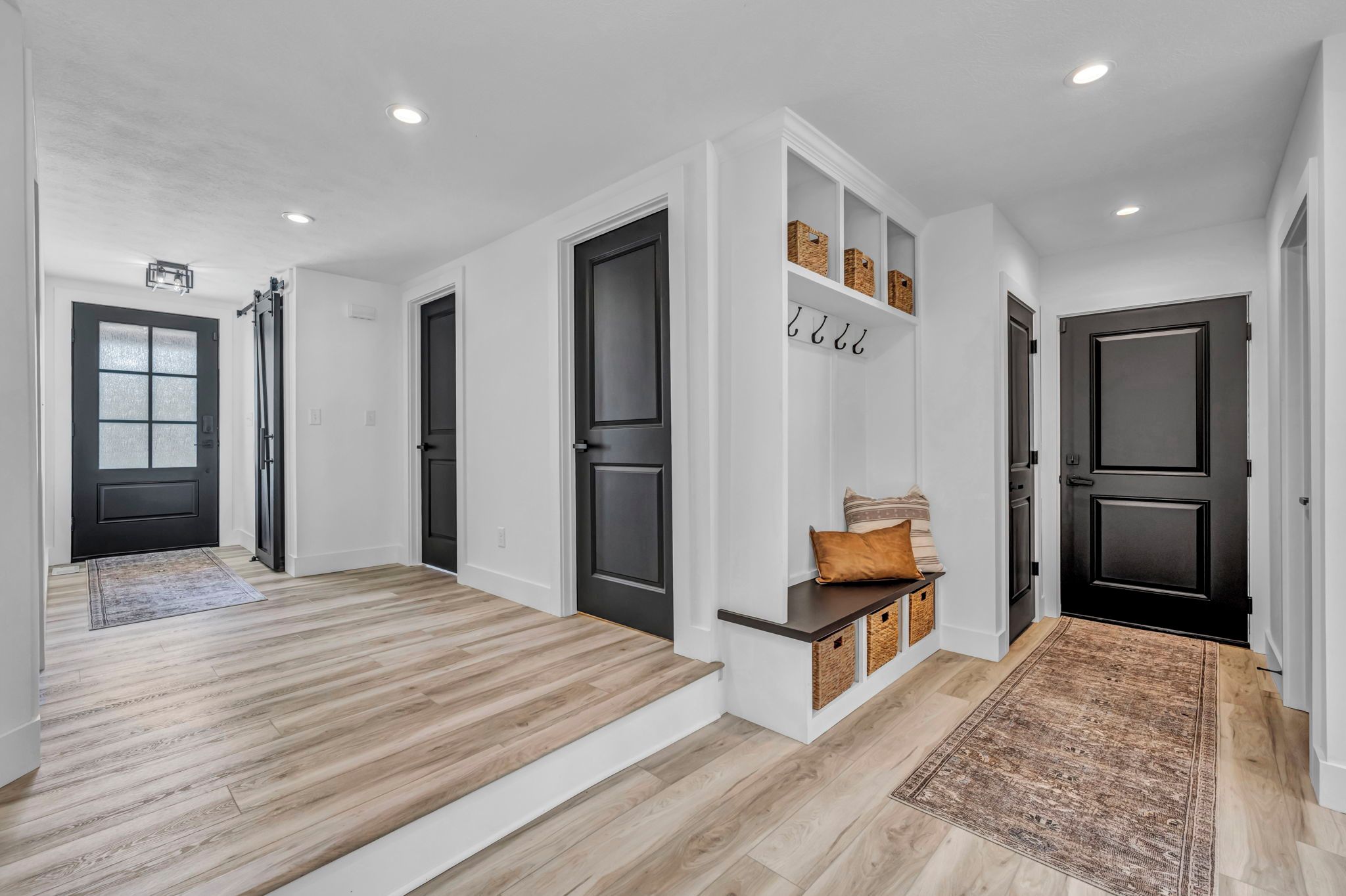 A modern interior with a wooden floor, black doors, and a bench with baskets.