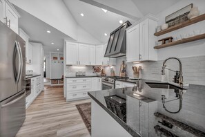 Une cuisine moderne avec des meubles blancs, un îlot central, des appareils électroménagers en acier inoxydable et un four encastré.