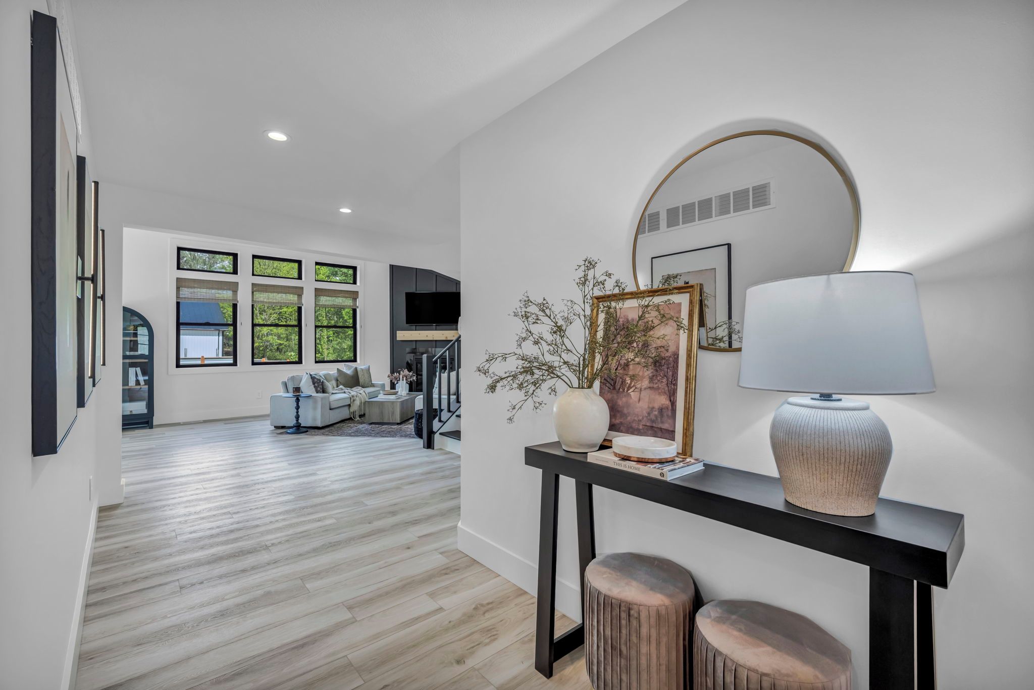 Un salon moderne avec un canapé, une console sur laquelle est posée une lampe, et une grande fenêtre donnant sur un paysage verdoyant.